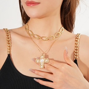 Close-up of layered gold cross pearl necklace and thick curb chain on model