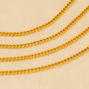 Close-up of four parallel 18K gold-plated stainless steel Cuban link chains on a beige background