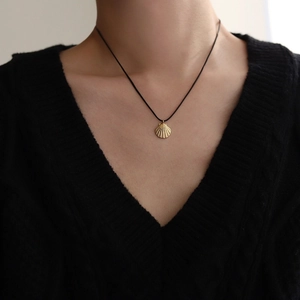Detail of golden shell pendant necklace with black cord worn on a model's neck