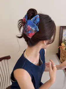 Détail d'un chouchou à nœud tie-dye bleu porté en chignon avec des bijoux en perles