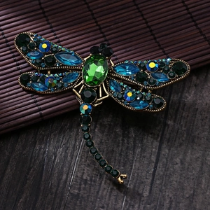 Detailed macro view of vintage gold dragonfly brooch with green emerald cut crystals