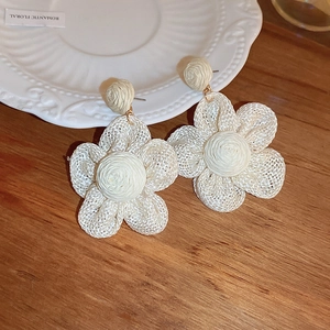 Close-up of bohemian cream woven raffia flower earrings with a textured spiral center