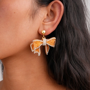 Detail of sparkling orange resin bow earrings with rhinestone fringe worn by model