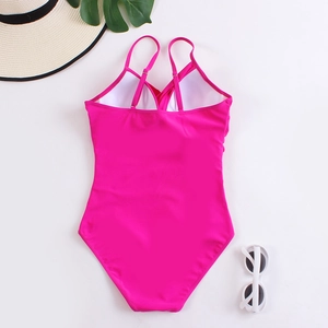 Detail of rose pink one-piece swimsuit featuring crisscross back straps and summer props