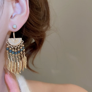 Macro shot of vintage bohemian gold tassel earrings with dark blue beads and feathers