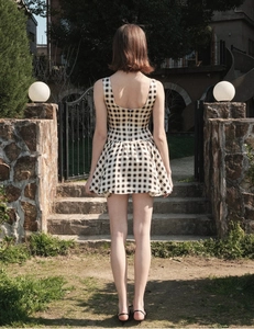 Rear view of a black and white plaid sleeveless mini dress in an outdoor garden setting