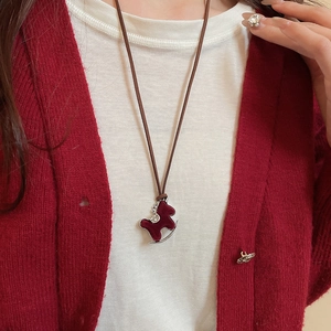 Close-up of a deep red flocked pony necklace worn by a model in a red cardigan