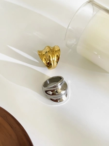 Polished wavy gold and silver stainless steel rings on a minimalist white table