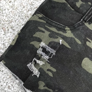 Detail der High-Waist Camouflage Denim-Shorts mit Distressed-Effekten auf weißen Steinen