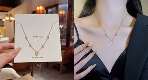 Detail view of a gold heart pendant necklace with zircon accents on a display card and model