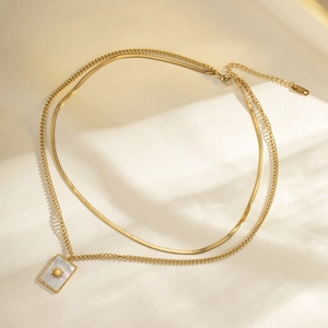 Detail of layered gold stainless steel necklace with sun pattern pendant and flat snake chain