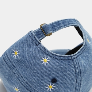 Detail of blue denim baseball cap featuring daisy embroidery and vintage brass buckle