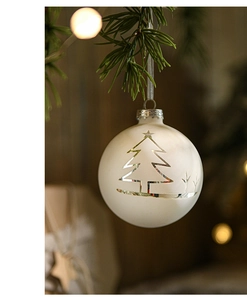Close-up of 8cm glass Christmas ball with white tree pattern hanging on pine branch