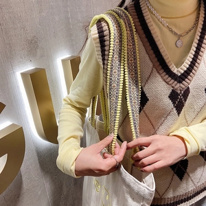 Detail of canvas tote bag with pompom strap paired with a knit vest and layered necklaces