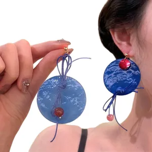 Blue marble texture round earrings with braided rope and red bead accents on white background