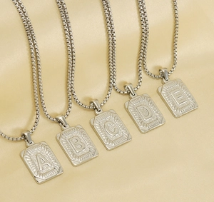 Close-up of square silver letter pendants A-E on box chains over gold silk background