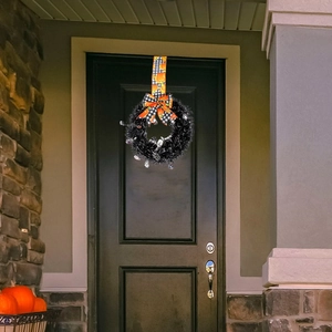 Close-up of Halloween wreath with black tinsel, pumpkin bow, and skulls on dark door