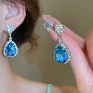 Dettaglio degli orecchini con pietre blu a goccia e castone a fiore con diamanti