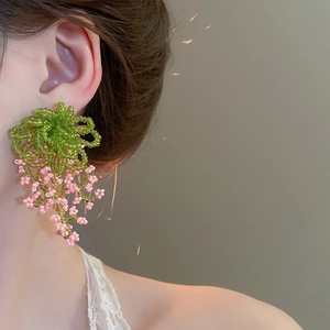 Detail of beaded floral tassel earrings featuring green leaves and pink berry clusters