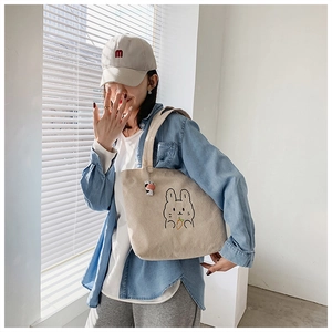 Detail of beige corduroy tote bag featuring a cute rabbit embroidery and soft texture