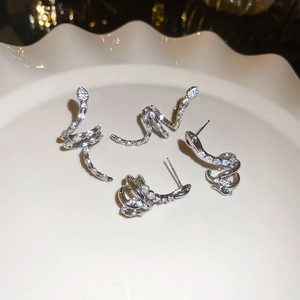 Detail shot of silver snake earrings with cubic zirconia on a white ceramic plate