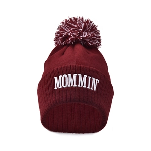 Detail view of burgundy knitted beanie with white MOMMIN embroidery and mixed color pom-pom