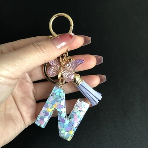 Detail of resin letter M keychain with purple butterfly, tassel and gold metal ring