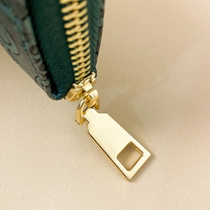 Close-up of golden zipper on dark green embossed leather wallet for women