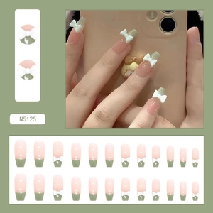 Detail of French style press-on nails in nude pink with green tips and white bows