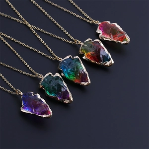 Macro detail of five rainbow crystal arrow pendants with gold chain on dark background