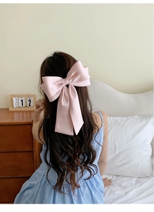 Rear view of a model wearing a large pink satin bow hair clip in an elegant half-up hairstyle