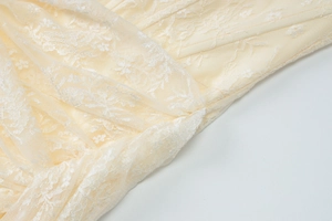 Dettaglio del tessuto in pizzo floreale beige con ricami intricati sul vestito