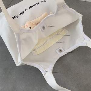 Detail view of white canvas tote bag featuring magnetic buckles and inner zipper pocket