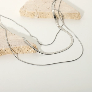 Detail of double-layer silver snake chain necklaces on beige stone decorative props