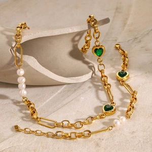 Detail of gold heart necklace with green gemstones and white pearls on stone background