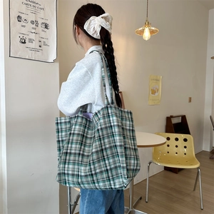 Detail of green plaid canvas tote bag with shoulder straps in a cafe setting