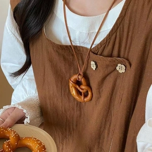 Macro shot of realistic pretzel pendant necklace with brown cord on a linen shirt