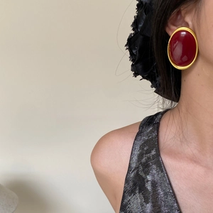 Close-up of retro oval red gemstone earrings with bold gold frames on model's ear