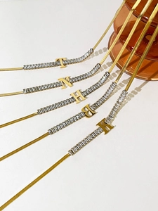 Detail of 18K gold plated snake chain necklace with zircon inlay and letter pendants
