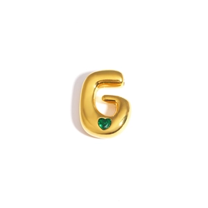 Détail d'un pendentif lettre G dorée avec une pierre précieuse verte en forme de cœur