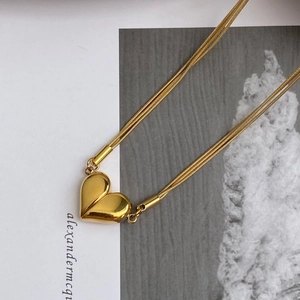 Detail view of double snake chain necklace featuring a gold polished heart pendant