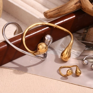 Detail view of 18K gold and silver water drop bangles on textured fabric and wood