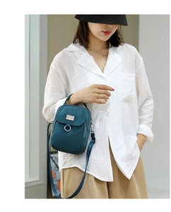 Detail of dark blue nylon crossbody phone bag with metal logo and zipper closure on model