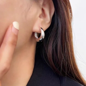 Orecchini a cerchio ovali spessi in argento lucido indossati da una modella donna elegante