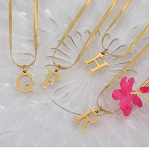 Detailed macro view of four 18K gold-plated snake bone necklaces with letter pendants