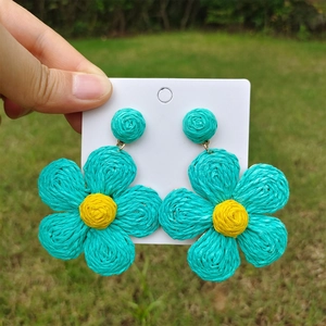 Detailed view of handmade woven flower earrings in blue and yellow on outdoor background