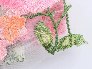 Vue macro de broderies florales sur tulle blanc avec motifs de fleurs roses et oranges