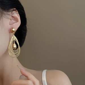 Golden multi-layer hollow teardrop pendant earrings worn by a model in a soft-lit studio