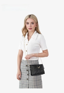Detail of black quilted shoulder bag with gold heart buckle worn by a model