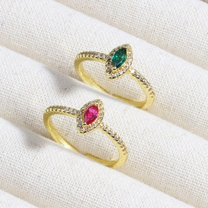 Close-up of gold rings with emerald and ruby marquise stones on beige fabric texture